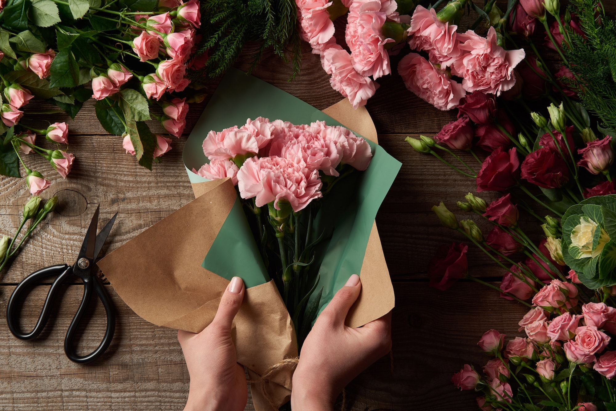 cropped shot of woman wrapping beautiful flowers in craft paper in wooden surface